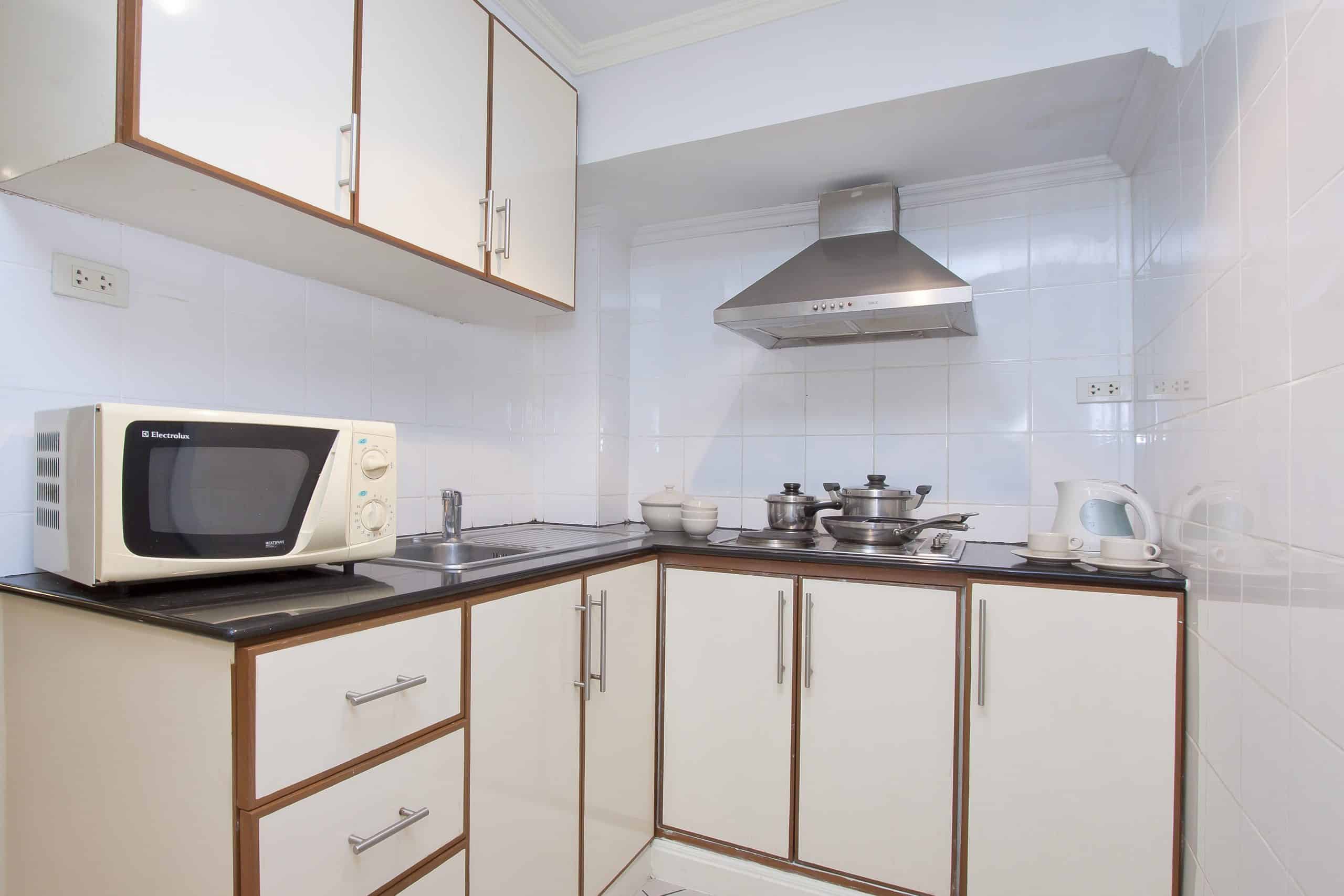 Well-equipped and functional Studio 10 kitchenette at Argyle Apartments in Pattaya, featuring a microwave and hot plate, cookware, dishes, utensils, and a small dining table with chairs