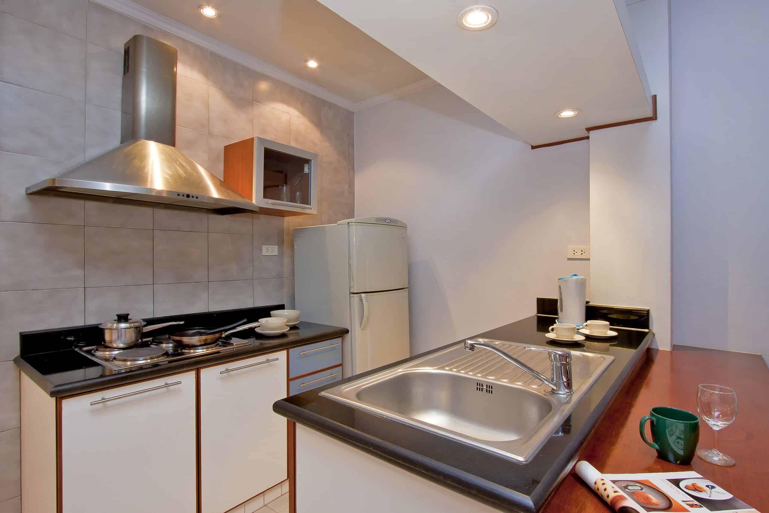 Well-equipped and functional Studio 10 kitchenette at Argyle Apartments in Pattaya, featuring a microwave and hot plate, cookware, dishes, utensils, and a small dining table with chairs
